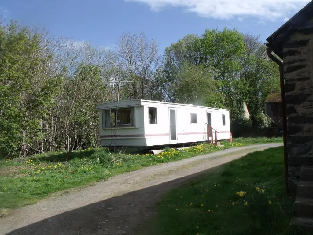 caravan nestled away amongst trees on edge of farm yard
