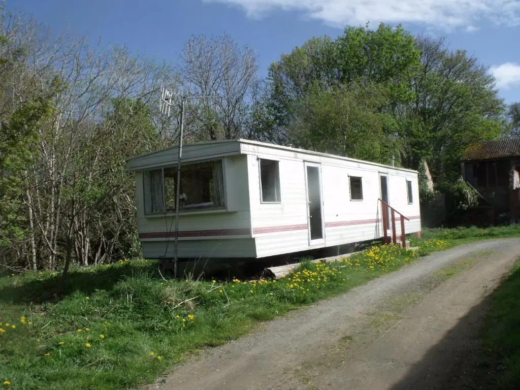 caravan nestled away amongst trees on edge of farm yard
